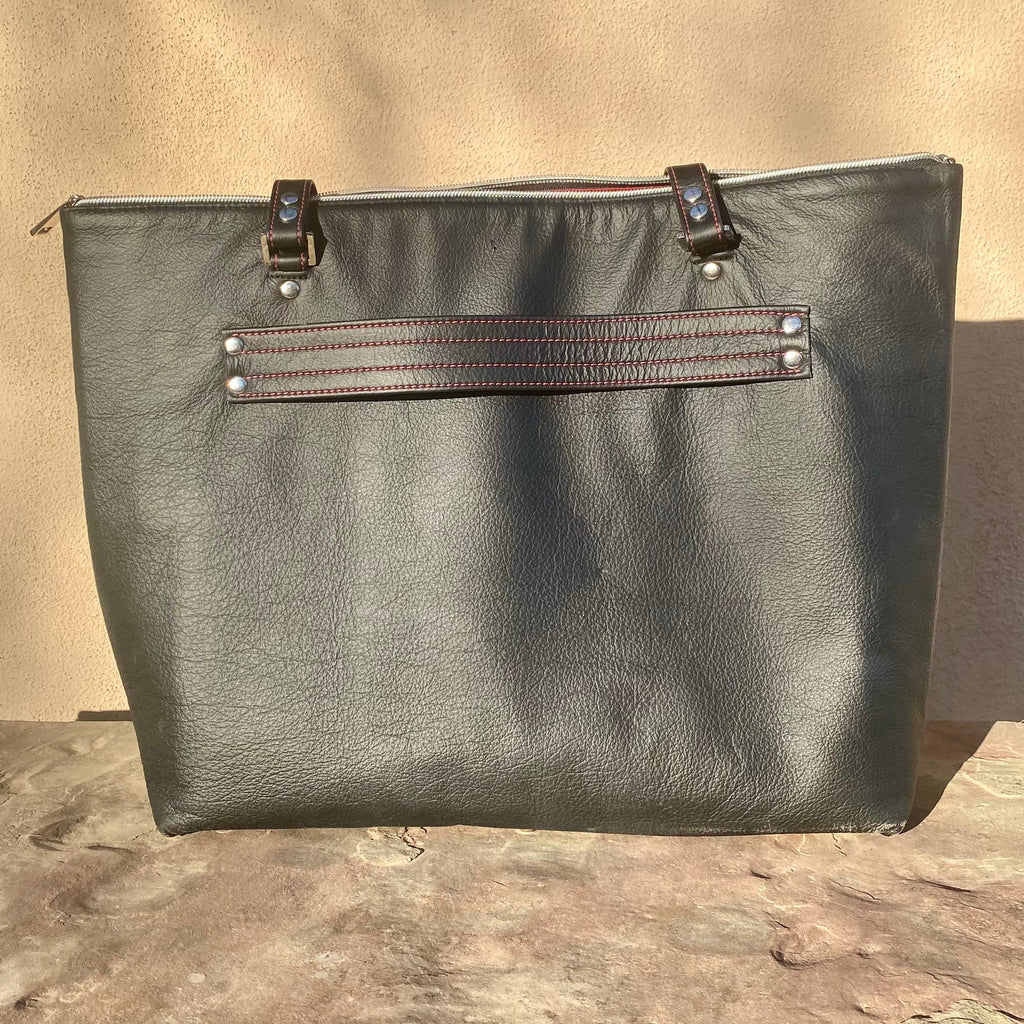 Black leather Luxora tote bag with strap for suitcase handle with red stitching on brown stone surface