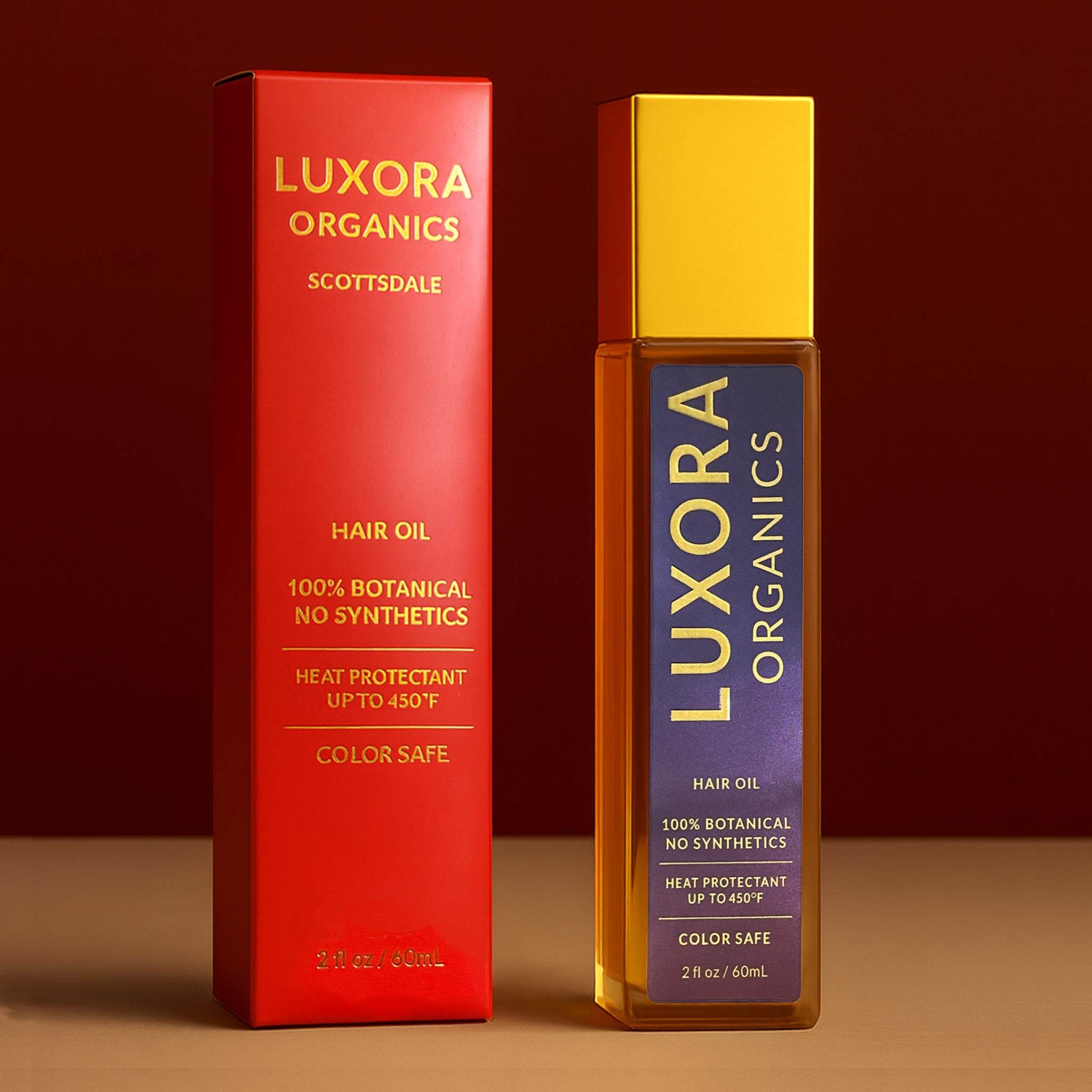 Luxora Organics hair oil glass bottle  with purple sticker with gold writting. Glass bottle also has a gold top. On side of bottle is red packaging with gold writing. The table is  light brown and background  is a burgundy color. 60 ML size bottle