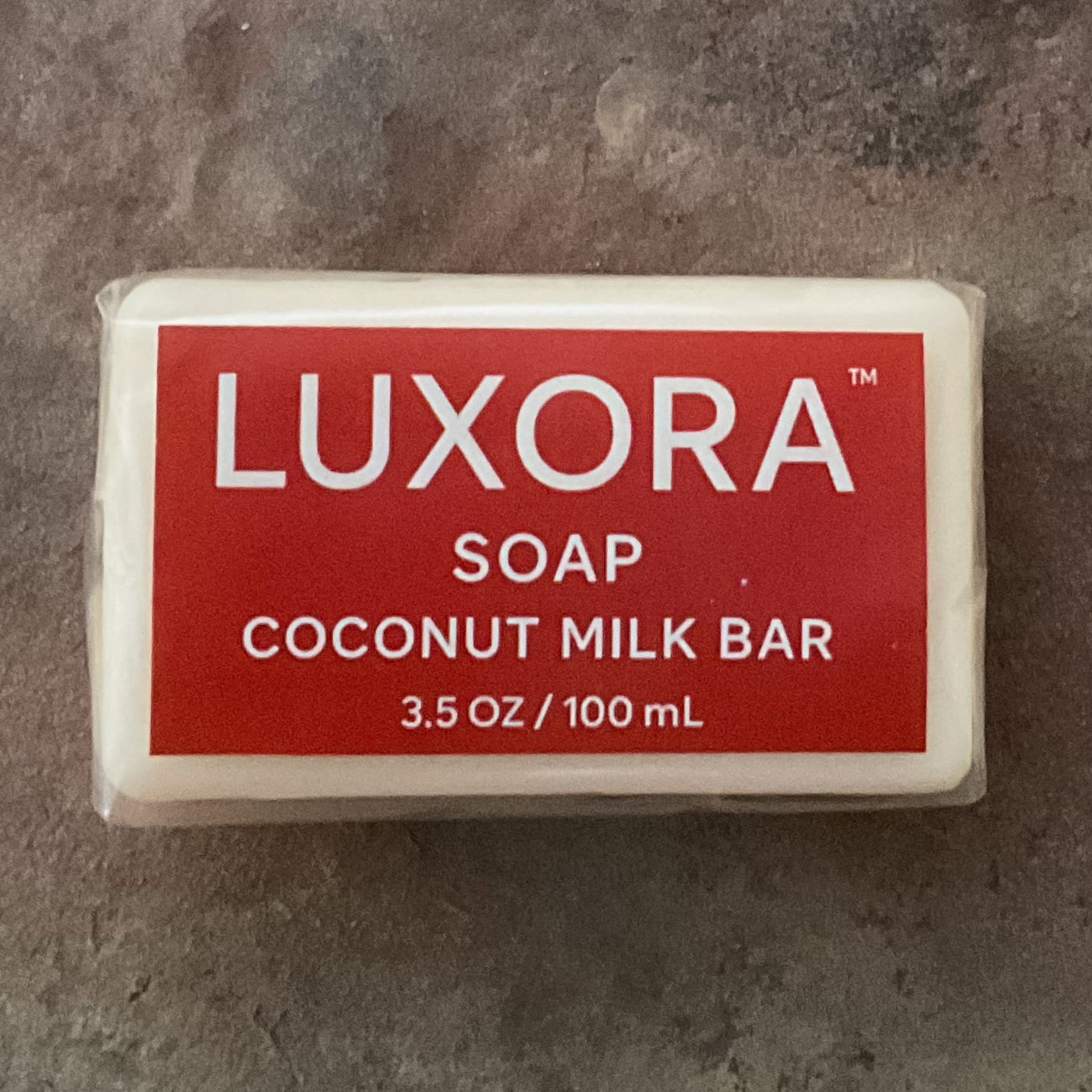 White bar of soap with red label, Luxora coconut milk bar soap on a brown and grey stone surface